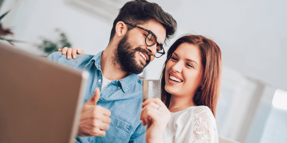 Man using laptop and woman holding credit card smiling after paying off credit card debt