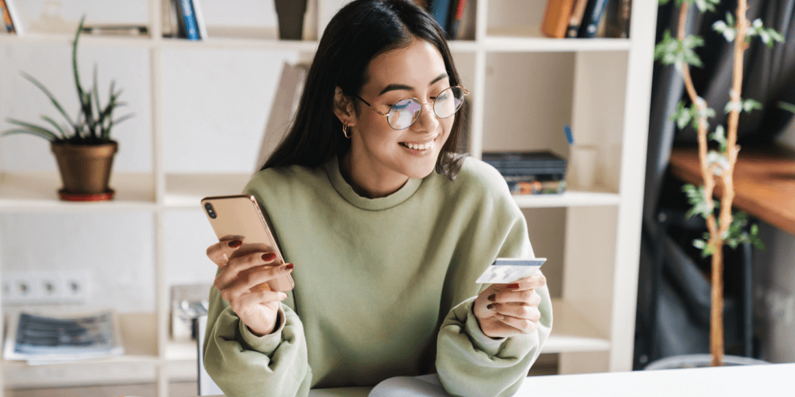 A person surrounded by schoolbooks and researching how to build credit as a college student on her phone