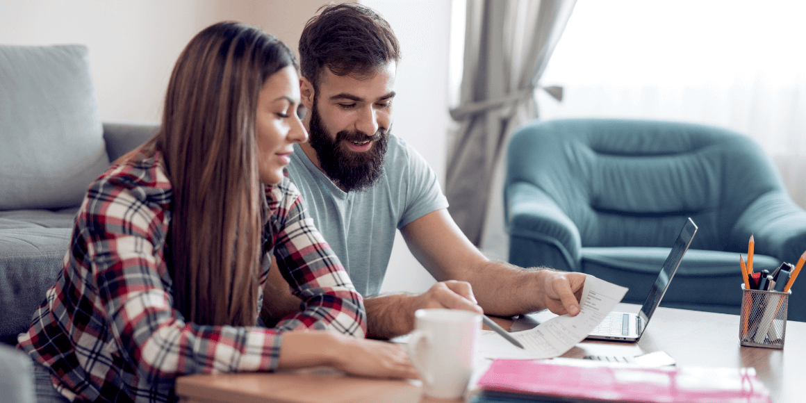 A couple sitting on their couch and looking at financial documents together.
