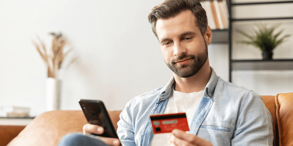 A man sitting on a couch and inputting debit card details on his phone.