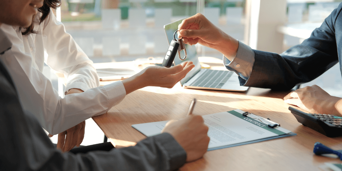 Salesperson handing over car keys while a couple finalizes their paperwork