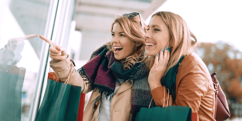 two women walking window shopping while holding shopping bags