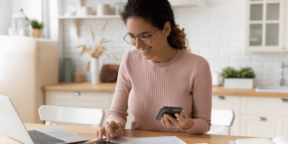 Woman calculating her taxes while sitting at a table with financial documents and a laptop in front of her