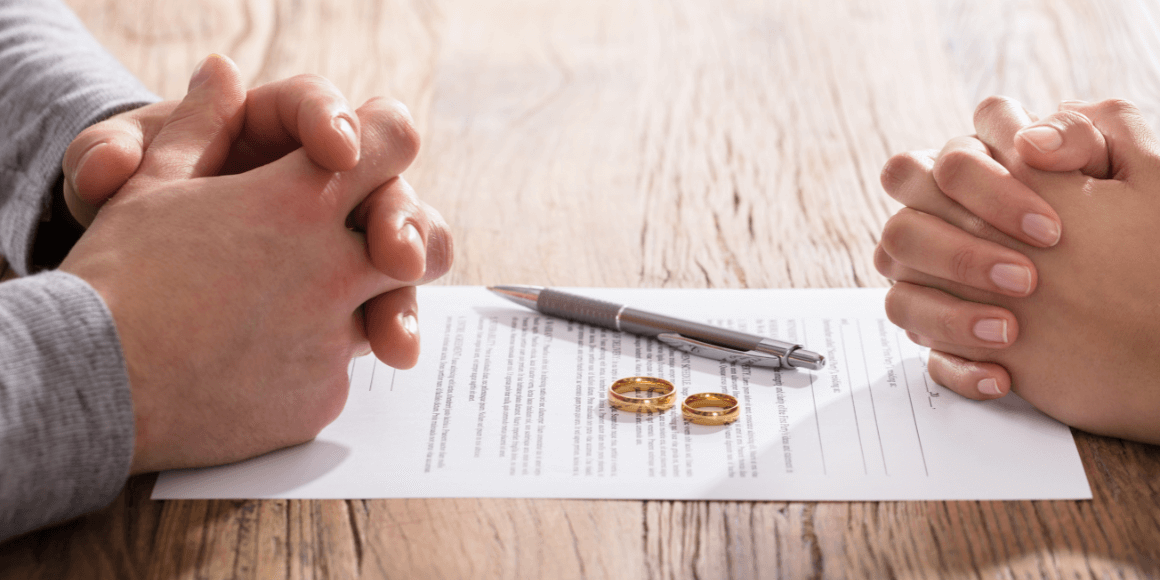 A couple sitting across from one another with a divorce paper in between them and their wedding rings on top of the paper. 