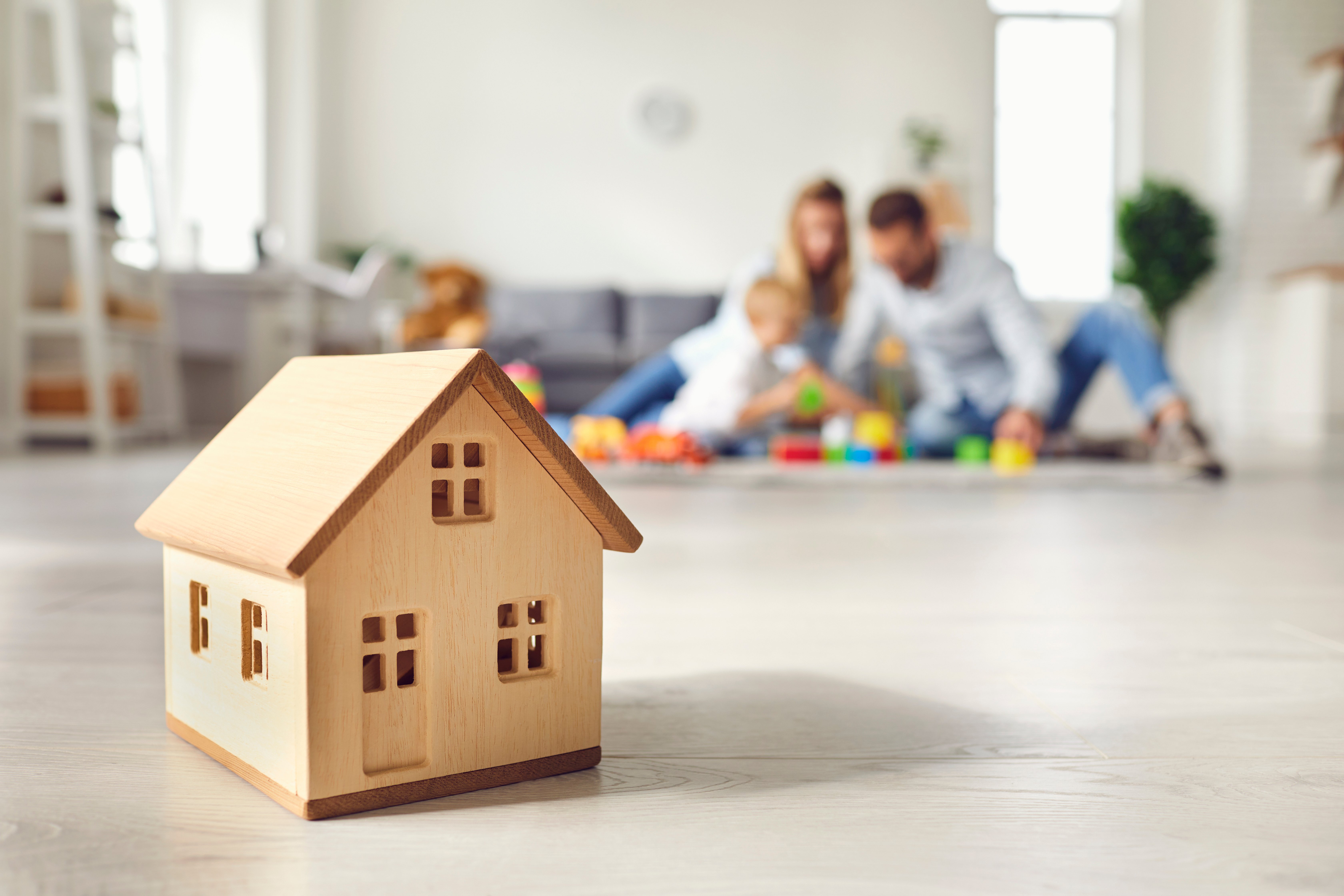 Little wooden house on floor of cozy room with happy family playing in background