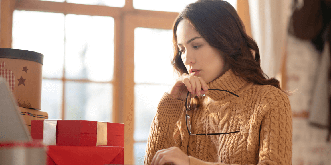 Woman in a cozy knitted sweater sitting at a table, engaged in holiday budgeting. 