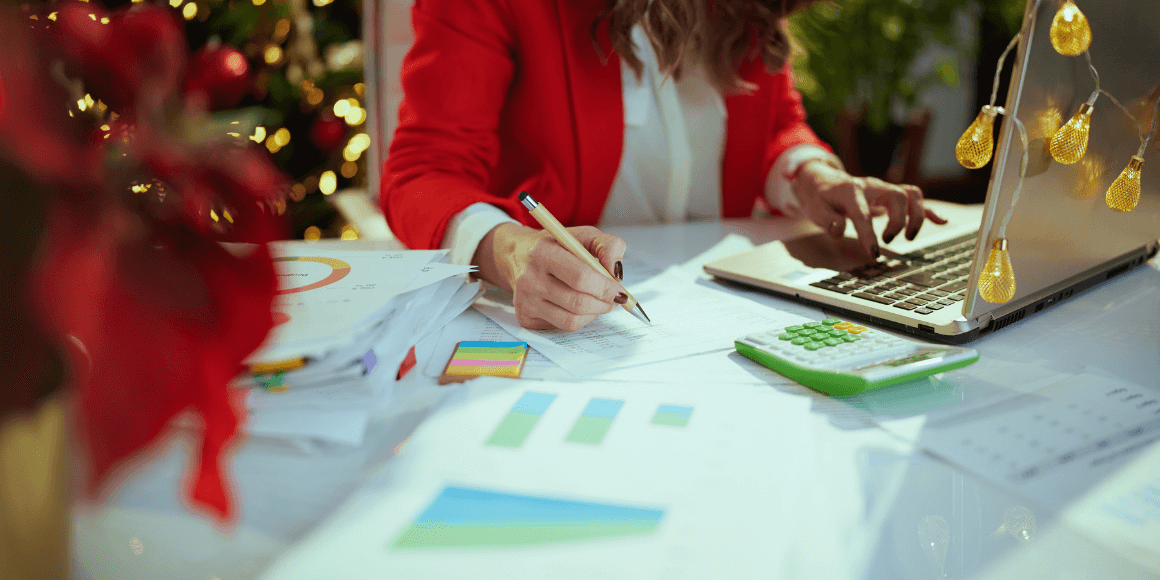 oman at the computer surrounded by charts, graphs and a calculator surrounded by holiday decorations which insuate’s that she is budgeting for the holidays