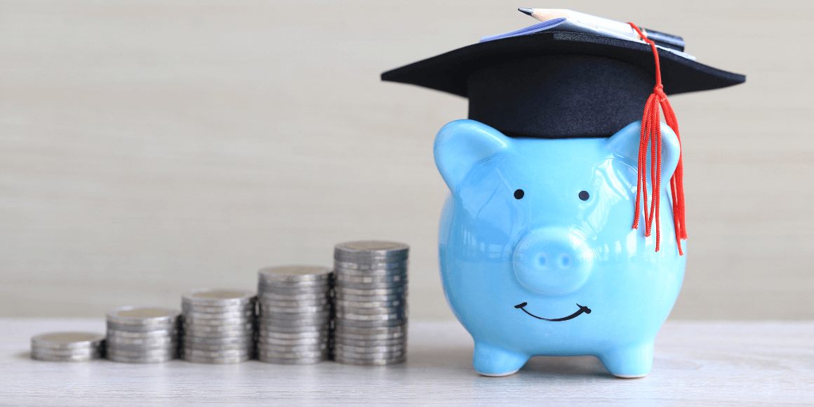 A blue piggy bank wearing a graduation hat next to a stack of coins