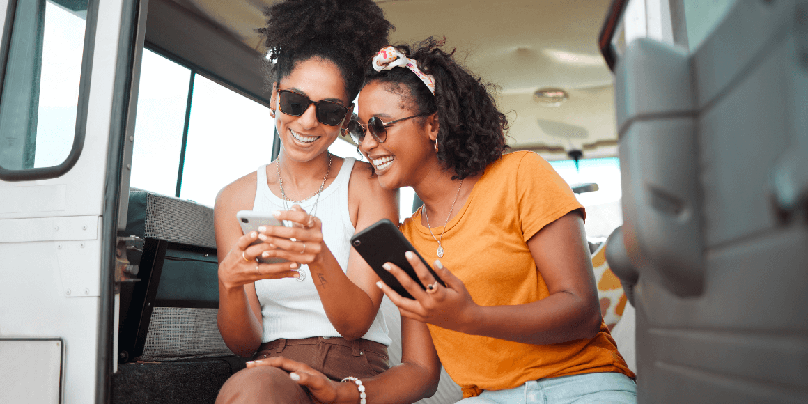 Two happy women looking at their phones on a roadtrip 