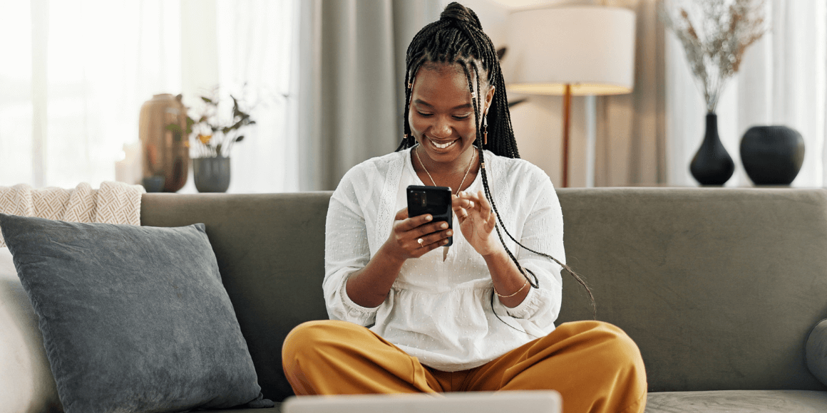 young black woman sitting on her couch while using the mobile banking app to review her finances