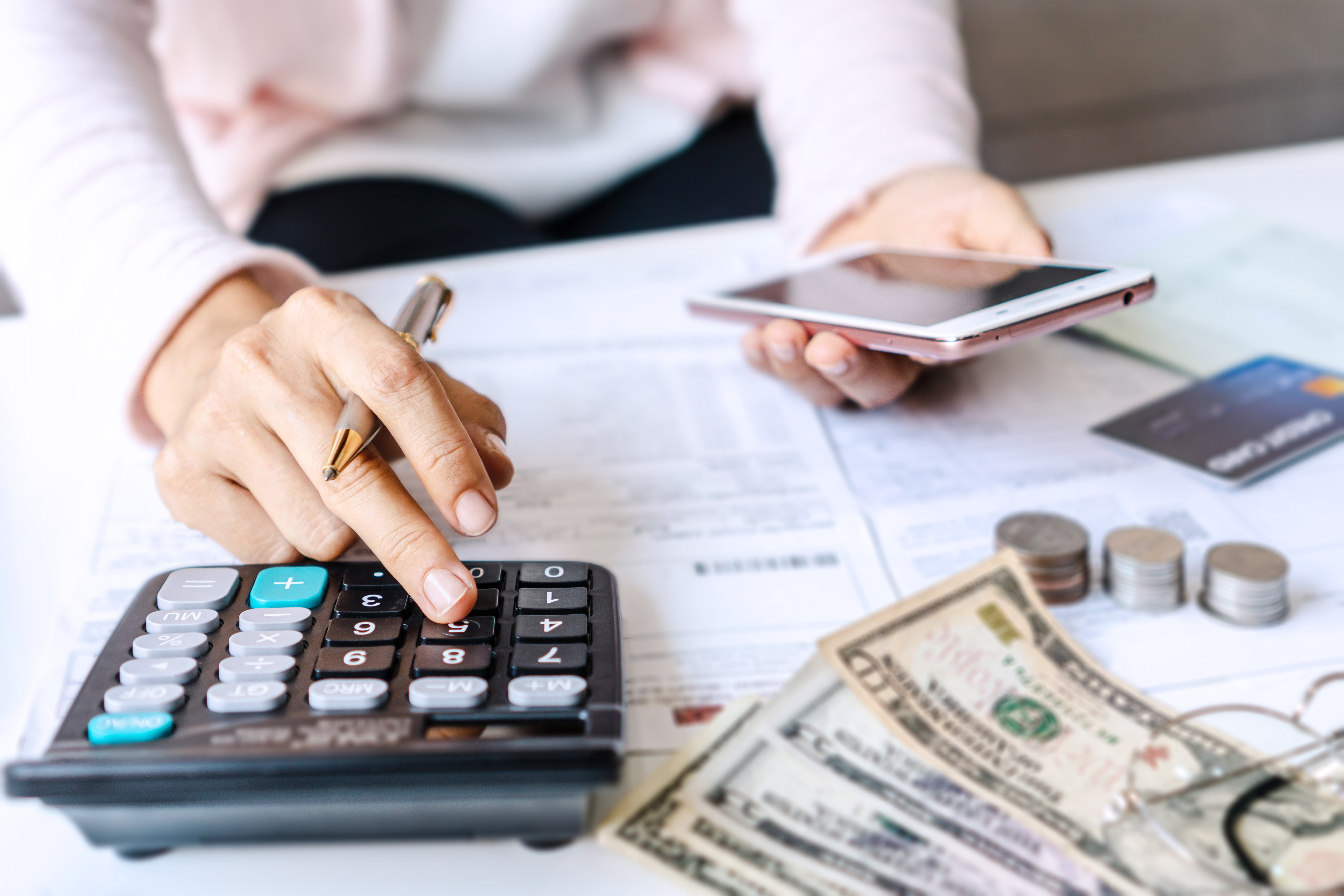 Closeup of a person holding a smartphone while using calculator for money management