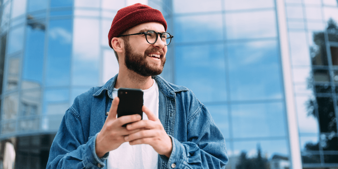 Man standing outside happily accessing the banking app on his phone