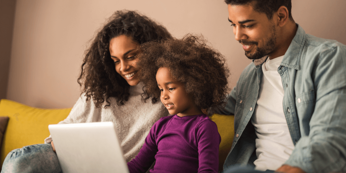 Two parents sitting on the couch with their child while holding a laptop