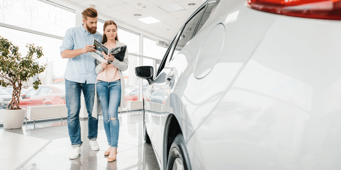 A couple reviewing a catalog while walking around a car dealership and buying their first car