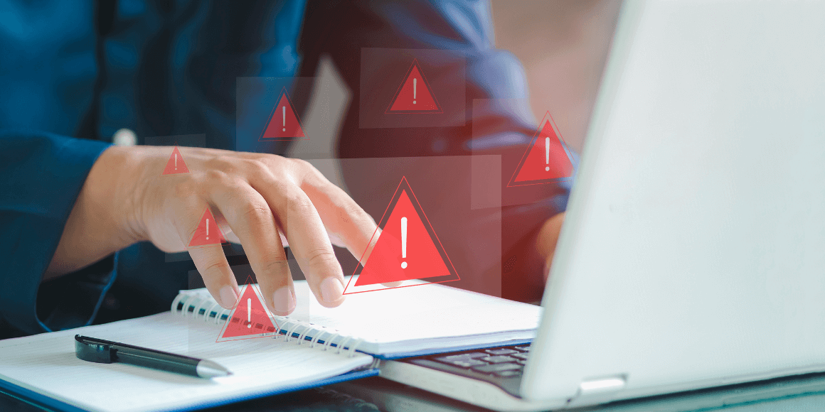 Man sitting in front of their laptop and an open notebook with red warning symbols 