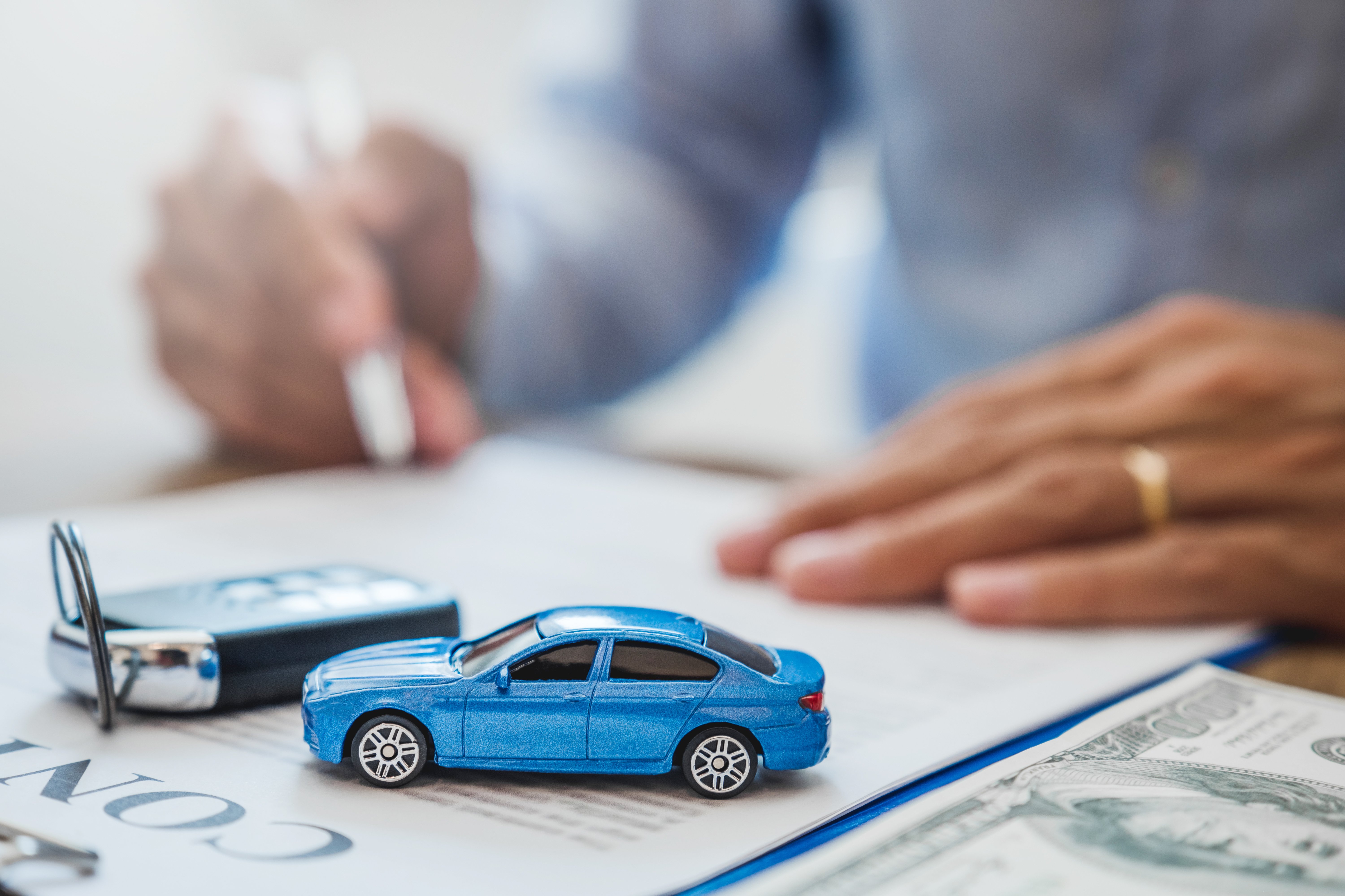 A closeup of a toy car and real car keys on top of auto loan refinancing paperwork